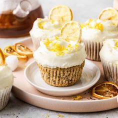 cupcakes with lemon and white frosting on a plate next to some orange slices