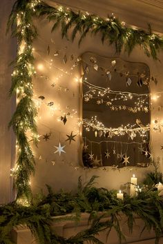 a fireplace with christmas lights and garland on it's mantle, next to a mirror