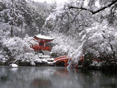 a red building sitting on top of a lush green forest next to a lake covered in snow