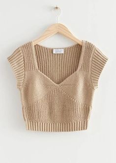 a cropped sweater hanging on a hanger with a white wall in the background