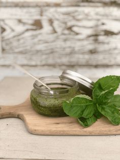 a wooden cutting board topped with jars filled with green liquid and fresh basil leaves next to it