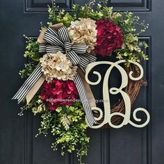 a monogrammed wreath with flowers and a bow hangs on the front door of a home