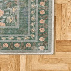 a green rug with pink flowers and leaves on the floor next to a wood floor