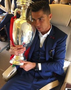 a man in a blue suit holding a silver trophy and looking at the camera while sitting on an airplane