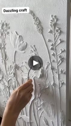 someone is painting the wall with white paint and flowers on it, while another person holds a