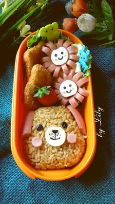 an orange container filled with rice and some animal faces on it's side, along with other food items