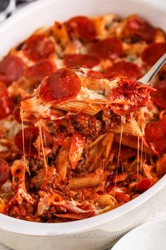 a large white casserole dish filled with pepperoni and cheese pizza sauce being lifted from the casserole