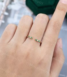 a woman's hand with a gold ring and emeralds on it, next to a green box