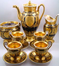 a gold and black tea set with matching saucers, cups and spoons on a white background