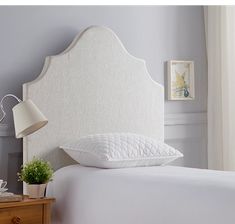 a white headboard with pillows on top of it in a bedroom next to a lamp