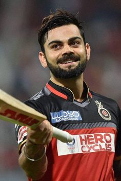 a man with a beard holding a cricket bat in his right hand and smiling at the camera