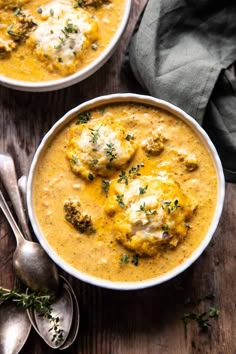 two bowls filled with soup on top of a wooden table next to silver spoons