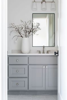 a white vase with some flowers in it on a bathroom counter top next to a mirror