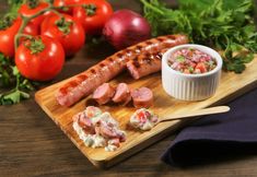 a wooden cutting board topped with meat and veggies next to a bowl of dip