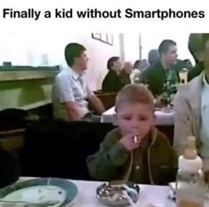 two young boys sitting at a table with food in front of them and an adult standing next to them