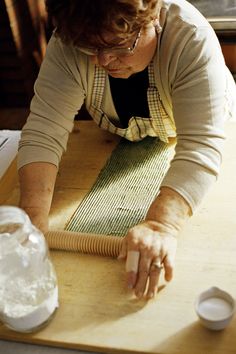 an older woman is making something out of paper on a cutting board with a knife