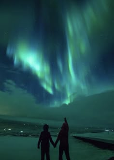 two people holding hands in front of an aurora bore over the ocean with bright lights