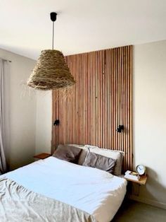 a bed with white sheets and pillows under a hanging light fixture in the corner of a room