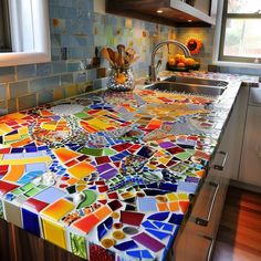 a kitchen counter covered in multicolored glass tiles and silver faucet, next to a window