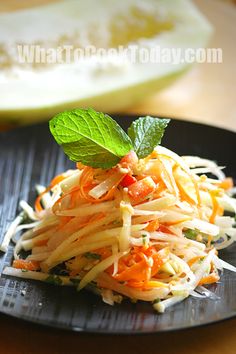 a black plate topped with shredded carrots and green leafy garnish on top of it