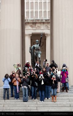 a group of people taking pictures in front of a building with a statue on it