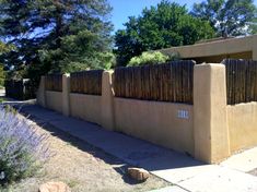 an adobe - style house with a fence in the foreground and lavender bushes on the other side