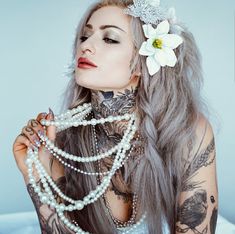 a woman with long grey hair and tattoos on her face, wearing pearls and beads