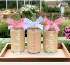 three mason jars with pink and white bows are sitting on a tray in the grass