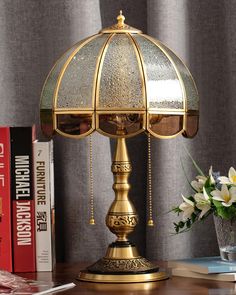 a gold lamp sitting on top of a wooden table next to a vase with flowers