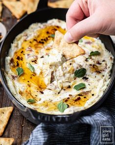 a hand dipping a cracker into a bowl of dip with pita chips on the side