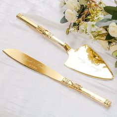 two gold - plated serving utensils on a white tablecloth with flowers in the background