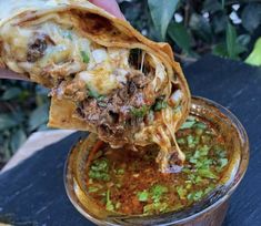 a hand holding a tortilla over a bowl filled with chili and meat soup