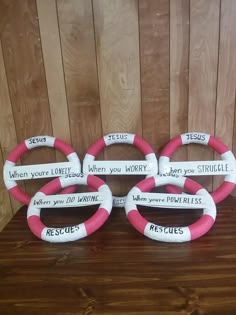 three pink and white life preservers with words on them sitting on a wooden table