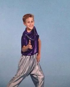 a young boy in purple shirt and silver pants posing for the camera with his hand on his hip