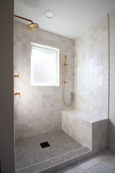 a white tiled bathroom with a window, shower head and bench in the corner next to it