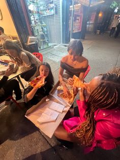 three women sitting on the ground eating pizza