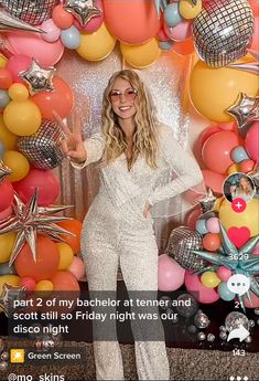 a woman standing in front of a backdrop with balloons and stars on it, giving the peace sign