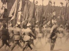 an old black and white photo of men in uniforms marching through the street with flags