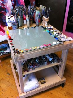 a table with lots of paint and brushes on it, in the middle of a room