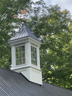 a tall white clock tower sitting on top of a metal roof next to green trees