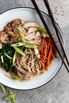 a white bowl filled with noodles and vegetables next to chopsticks on a table