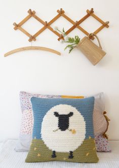 a crocheted sheep pillow sitting on top of a bed next to a coat rack