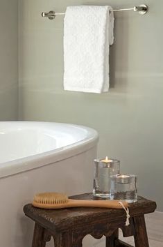 a white bath tub sitting next to a wooden stool with a toothbrush on it