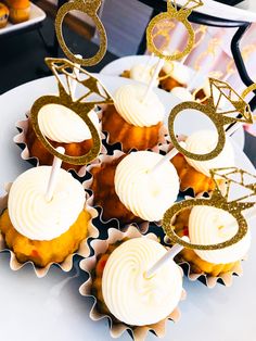 cupcakes with white frosting and gold glitter toppers are arranged on a plate