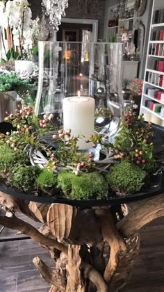 a table with moss and candles on it in front of a book shelf filled with books