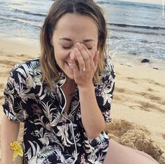 a woman is sitting on the beach with her eyes closed and she is covering her face