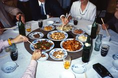 a group of people sitting around a table with plates of food and chopsticks