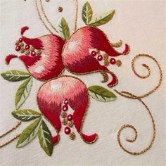 two pomegranates with green leaves and beads on a white fabric background