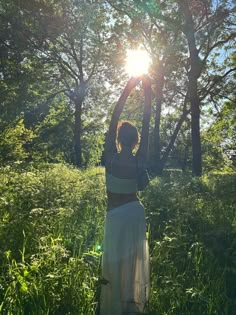 a woman is standing in the grass with her arms up to the sun above her head