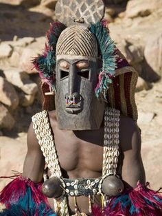 an african man wearing a mask and headdress in front of some rocks on the ground